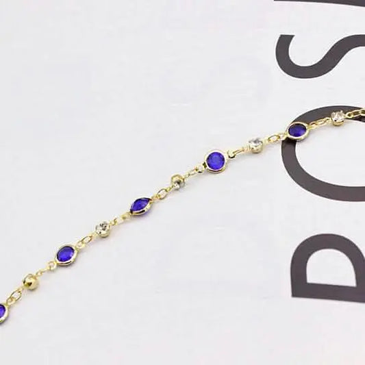 Gold-tone ankle bracelet close-up with blue crystal links and round connectors