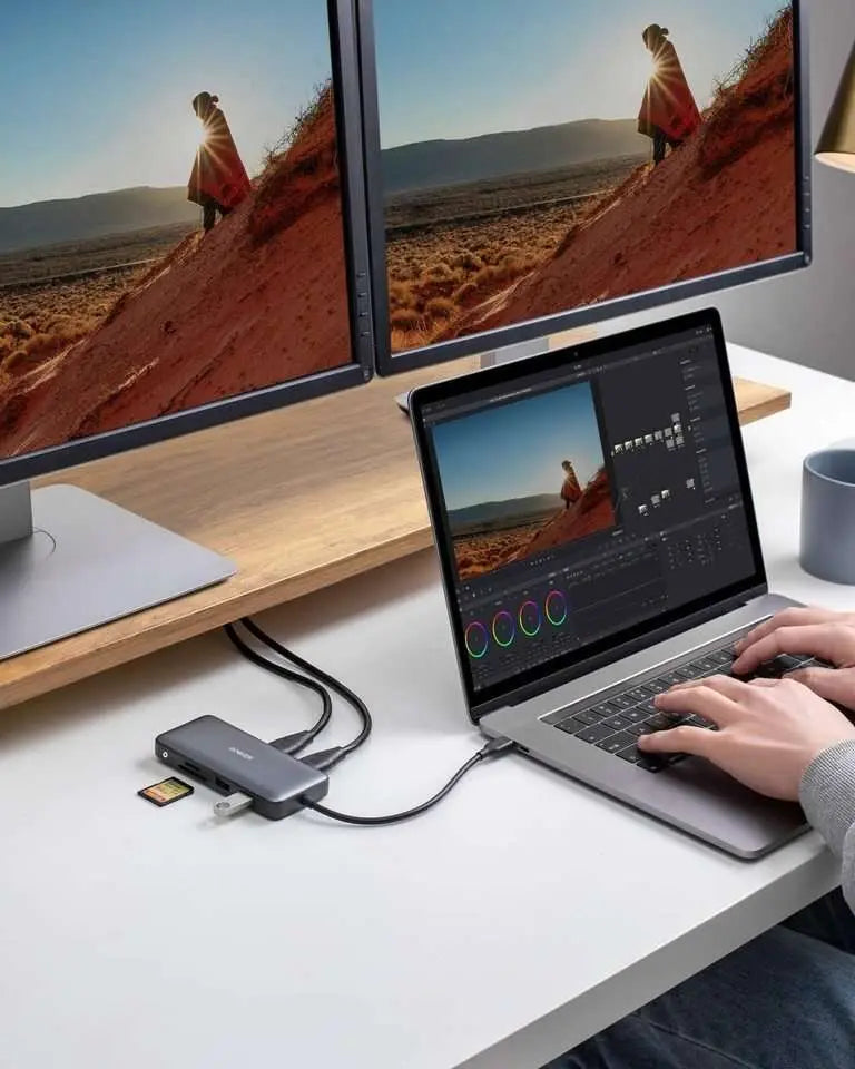 USB-C hub connected on a desk with dual monitors and a laptop running media