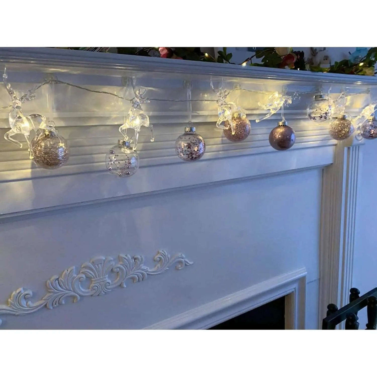 Warm white LED reindeer string lights hanging above a fireplace with glowing figures