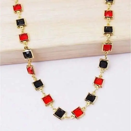 Gold-tone ankle bracelet with alternating red and black square beads, close-up