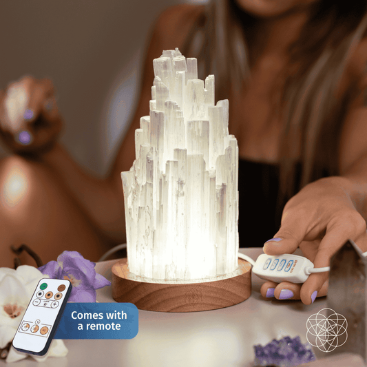 Selenite crystal lamp on a round wooden base with remote controls beside it, lit.