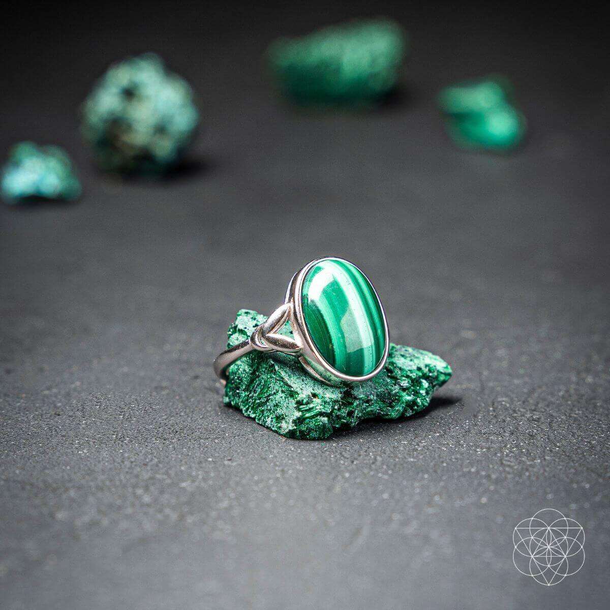 Green oval gemstone ring with silver setting on dark stone surface