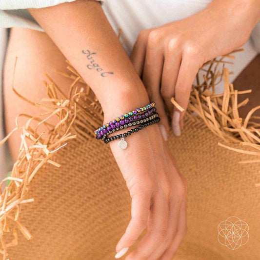 Stacked beaded wrap bracelets on wrist with purple, black beads, and a small silver charm