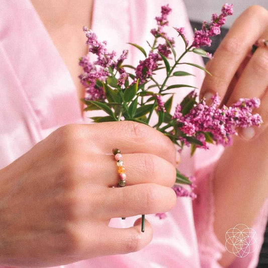 Multicolor beaded ring on finger with pink, green, and gold beads