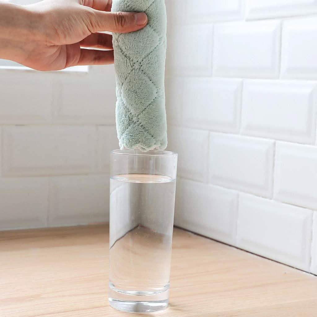 Teal dish towel roll standing in a clear glass container on a wooden counter
