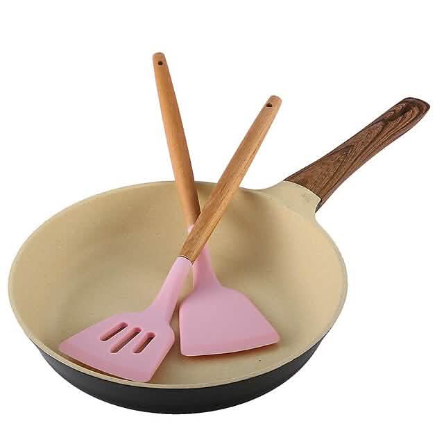Pink silicone spatula and slotted utensil with wooden handles in nonstick pan