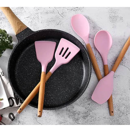 Pink silicone kitchen utensils with wooden handles, spatula pair over skillet
