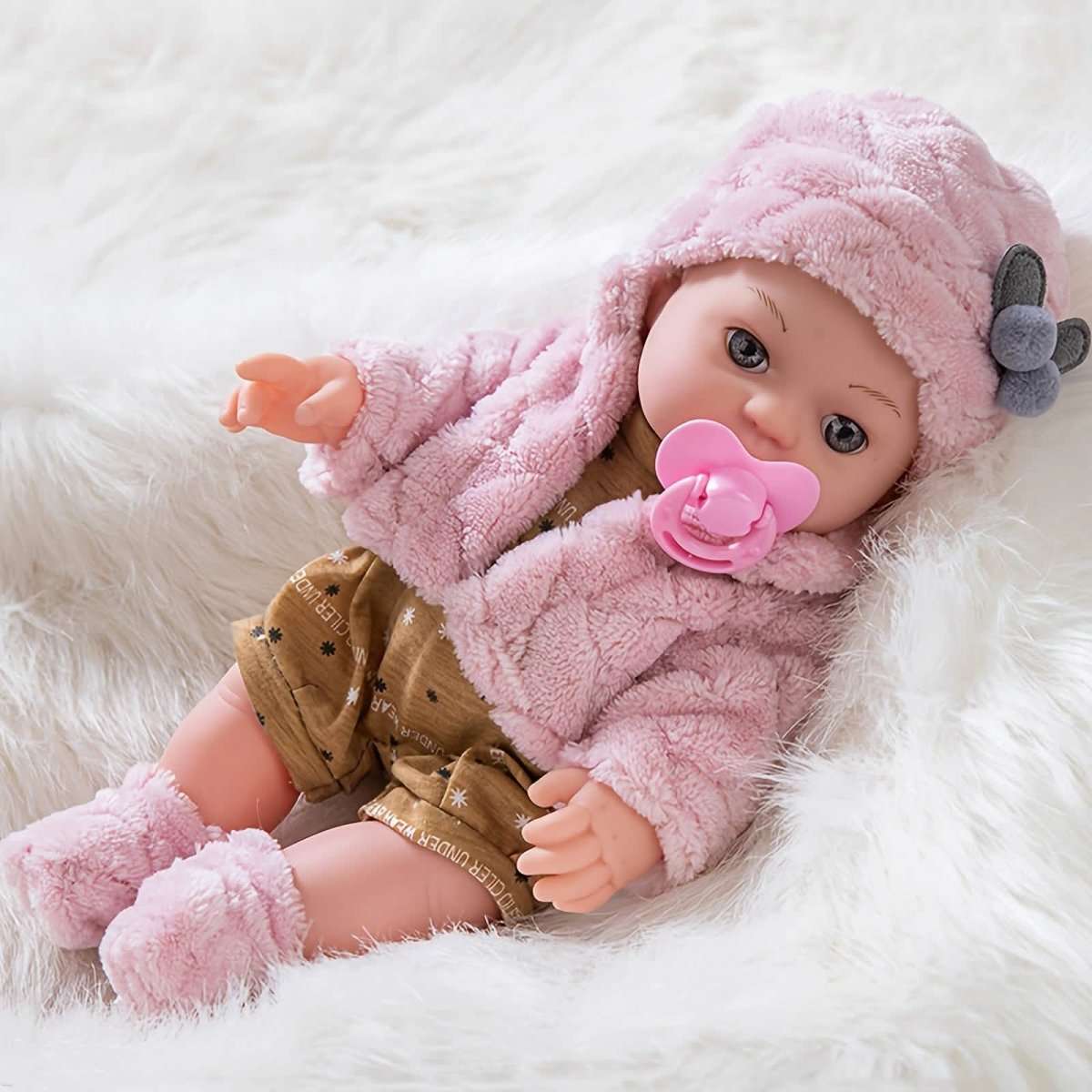 Pink plush baby doll lying down with gray ear hood, brown star romper, pink pacifier in mouth.