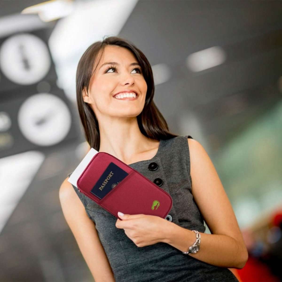 Travel passport wallet in maroon held in hand, with small green logo and zip closure.