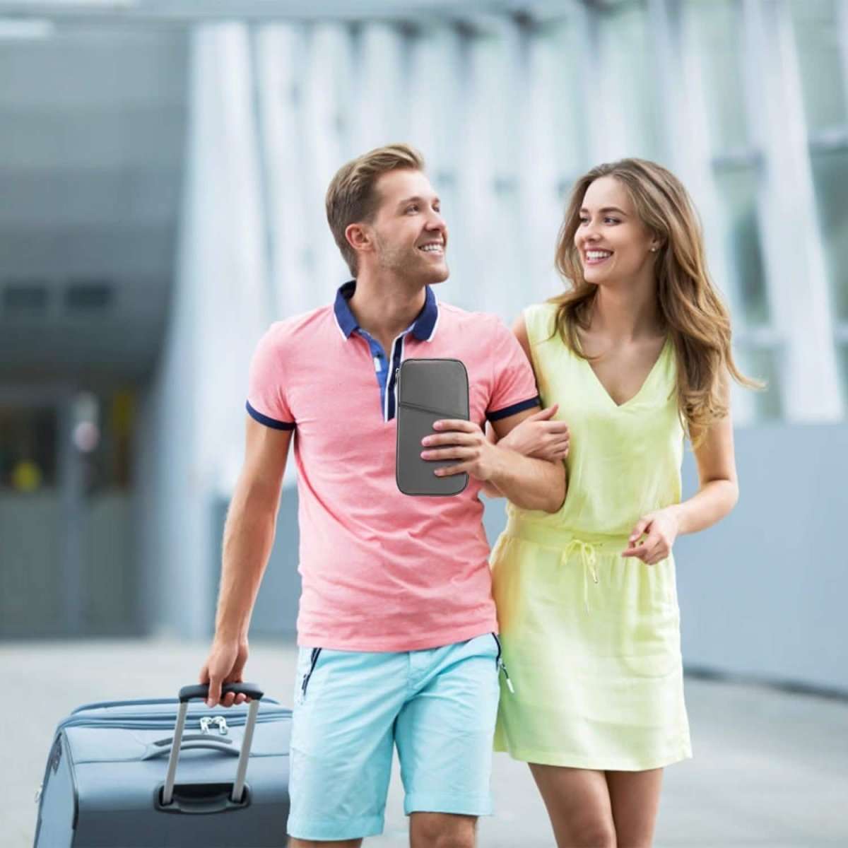 Travel passport wallet in dark gray/black held in hand over a trip bag