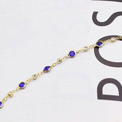 Gold-tone ankle bracelet close-up with blue crystal links and round connectors