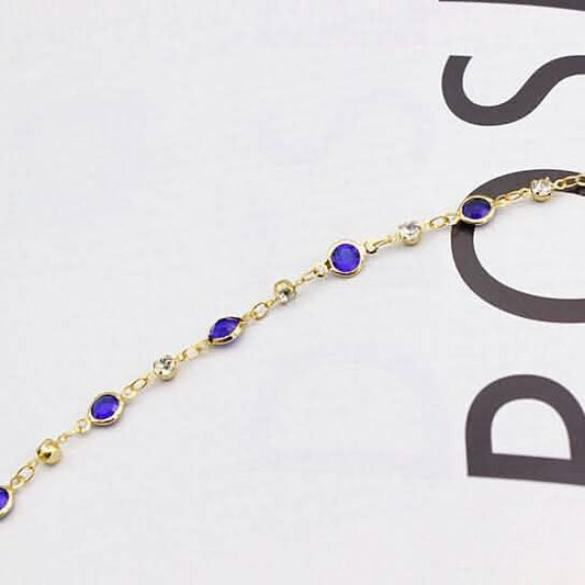 Gold-tone ankle bracelet close-up with blue crystal links and round connectors