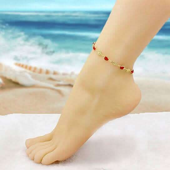 Gold-tone red crystal anklet on ankle with small flower charm stations