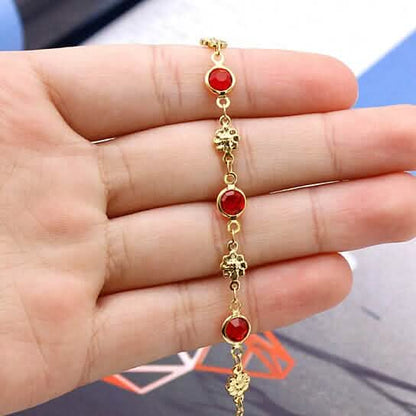 Gold-tone anklet bracelet held in hand, red crystal bezel links and flower charms