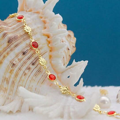 Gold-tone anklet with red round crystal beads and flower drop charms
