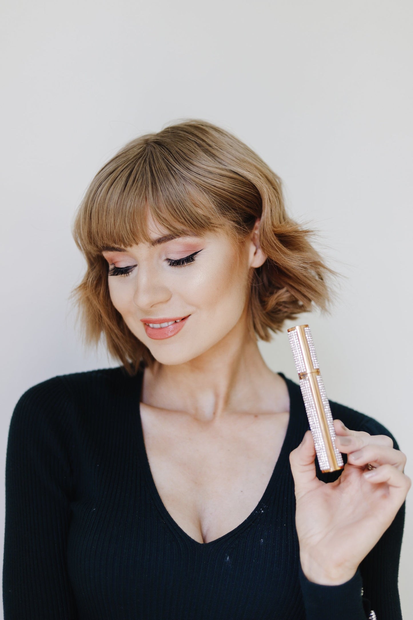 Model holding rhinestone mascara tube, eyes closed with visible lashes