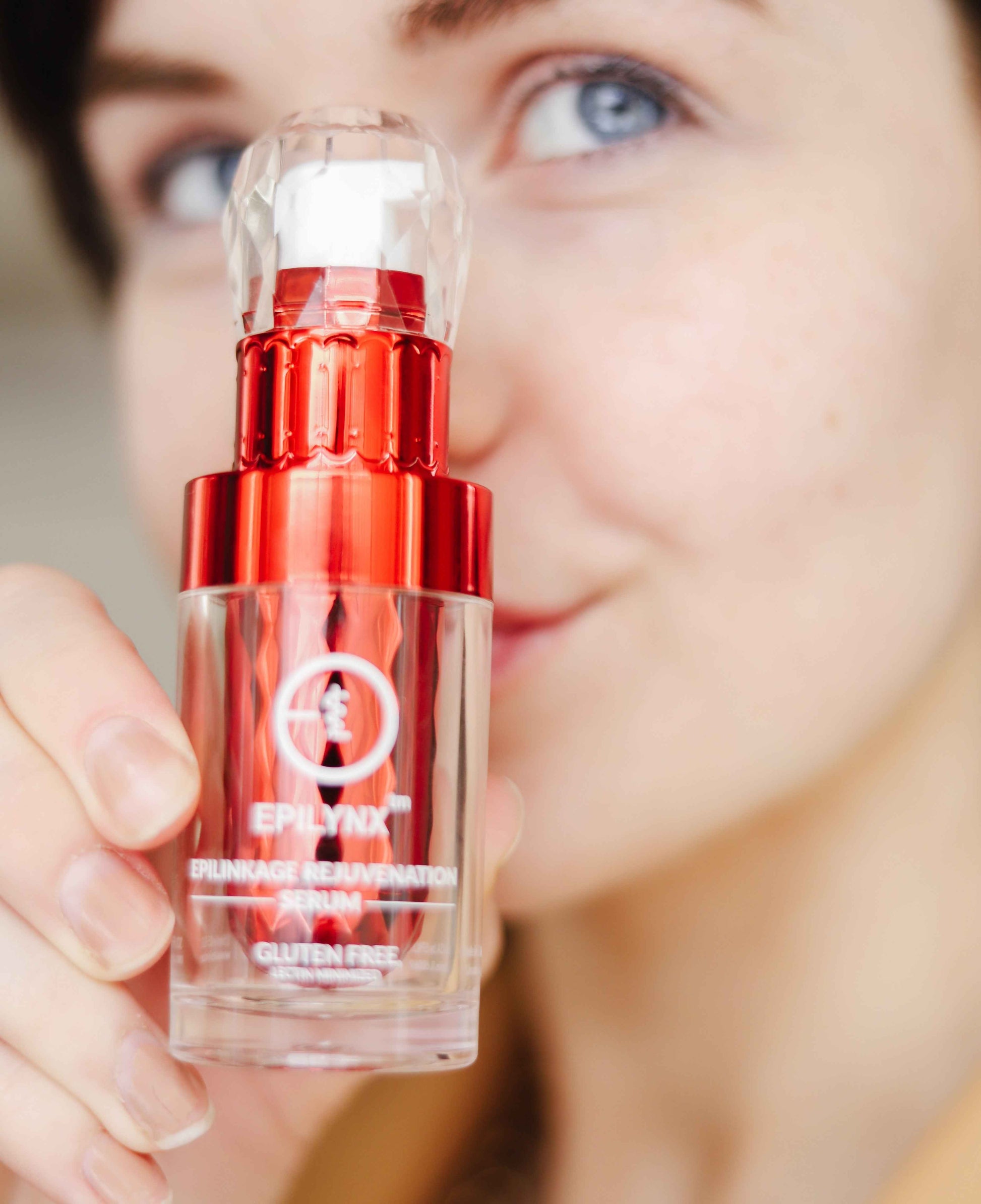Face serum bottle held in hand with red cap and clear glass body