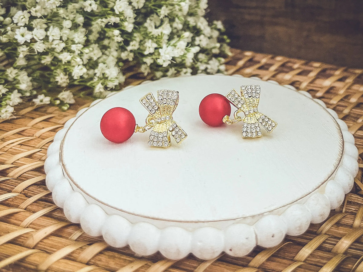 Gold-tone rhinestone bow ornaments with red ball drops on round white display