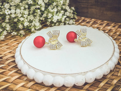 Gold-tone rhinestone bow ornaments with red ball drops on round white display