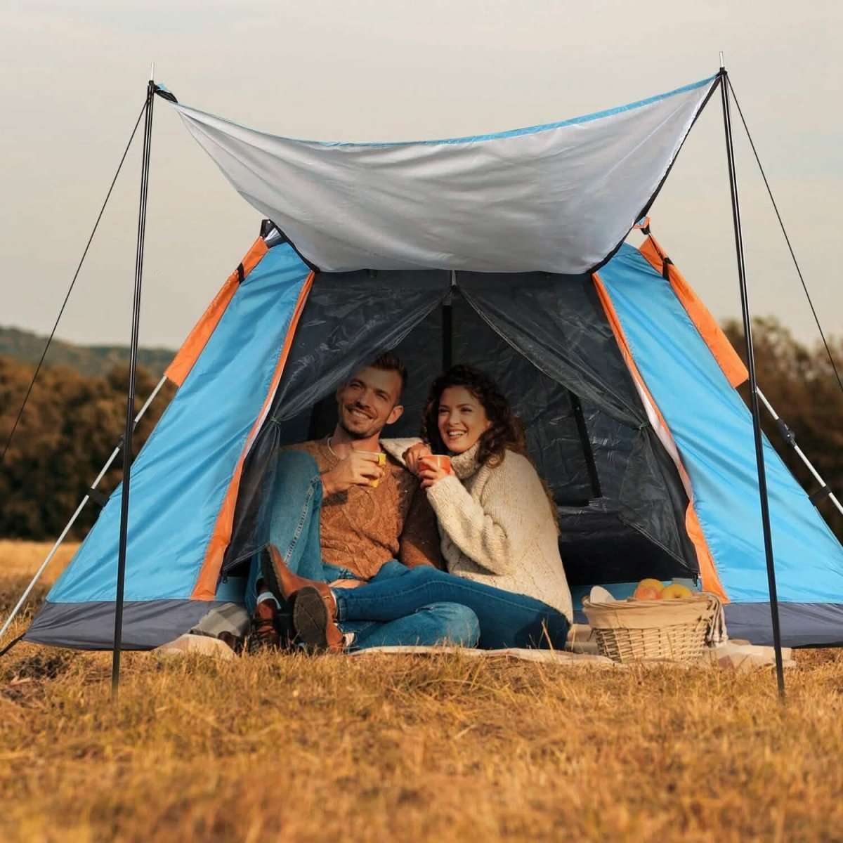 Blue 4-5 person camping tent with overhang; two people sitting inside under the canopy.