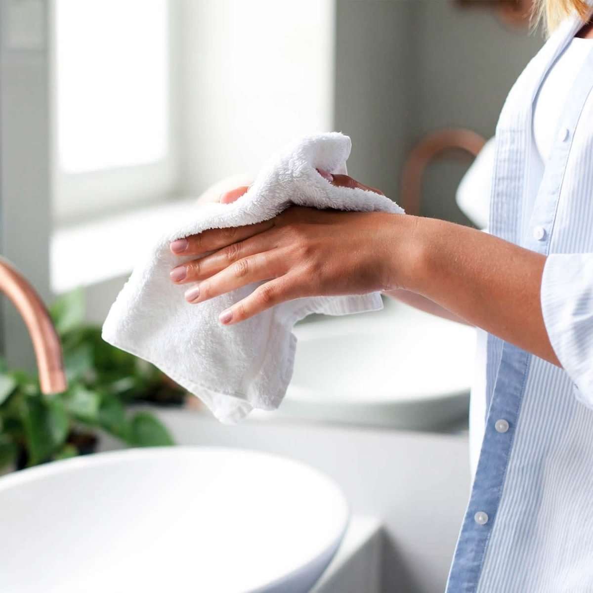 White bath towel folded in hands over a sink, soft terry fabric