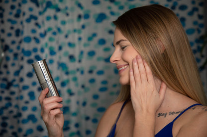 Face moisturizer bottle with chrome pump held by a woman near her cheek