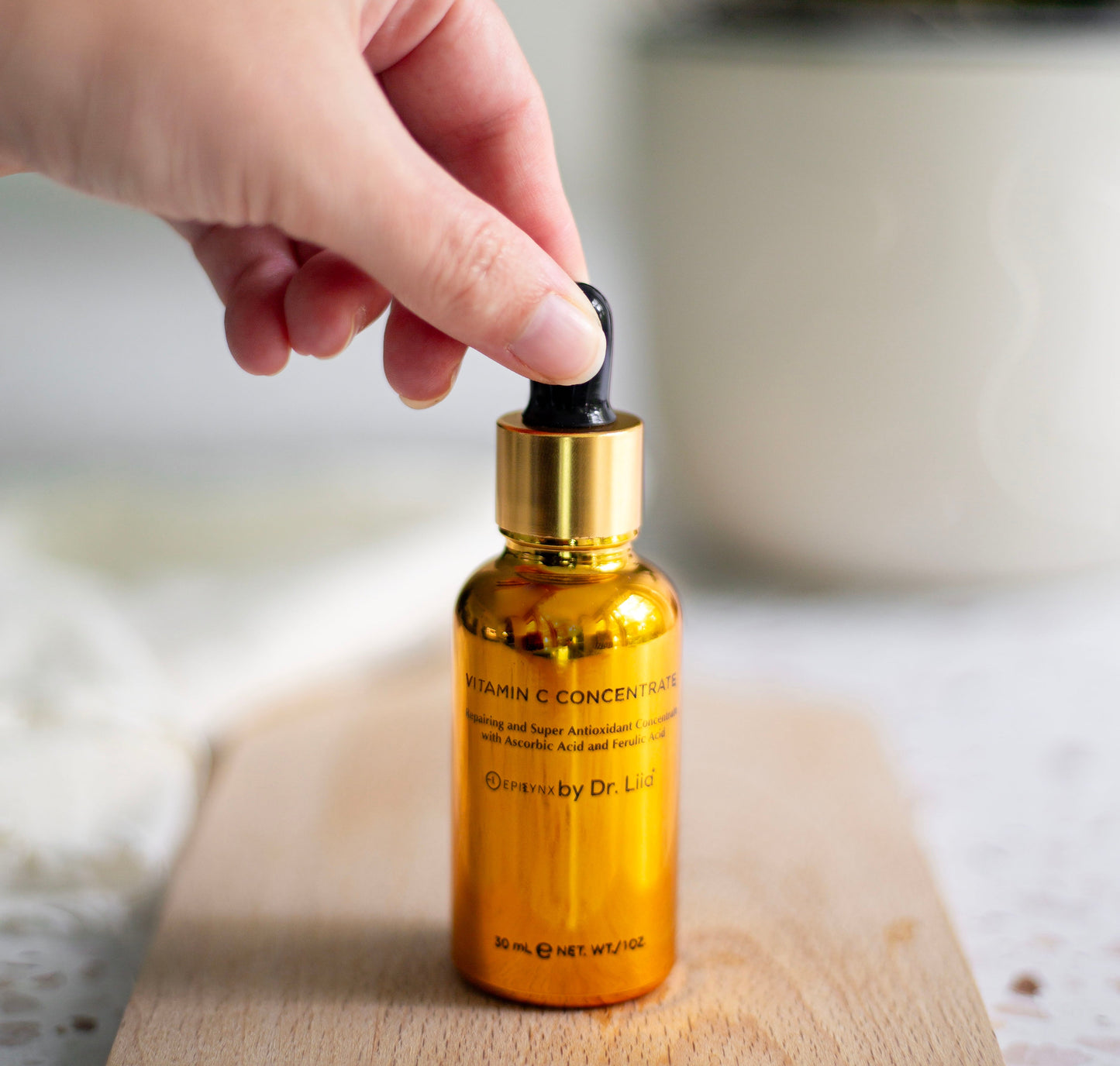 Golden serum bottle with black dropper tip held above the bottle opening