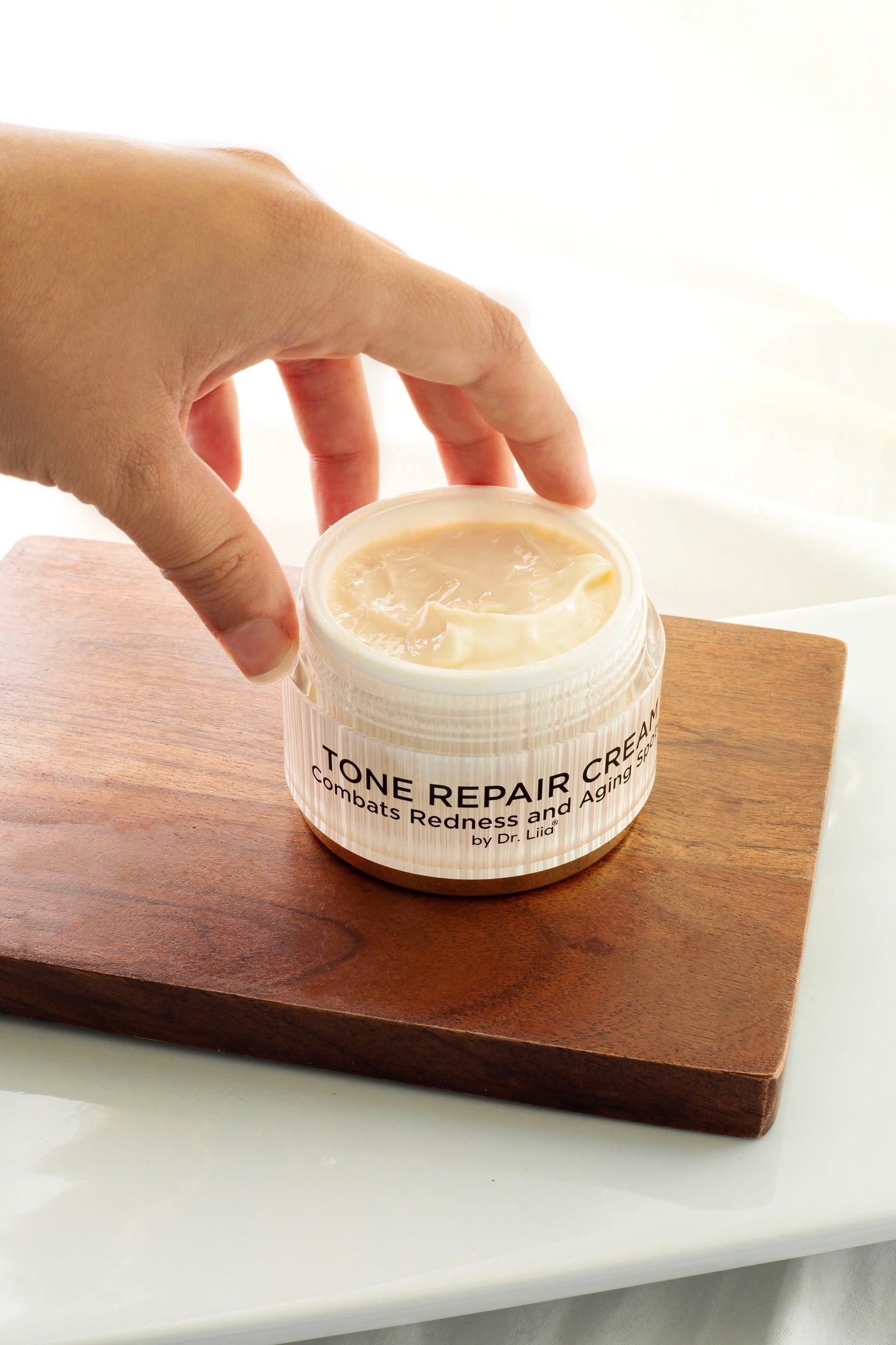 Tone Repair Cream jar held by hand, open lid showing pale cream