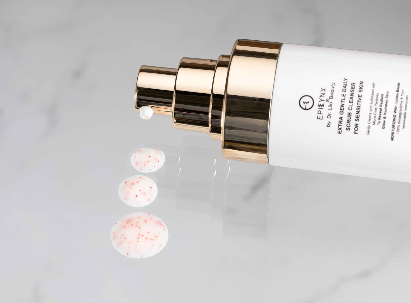 Skincare face scrub cleanser bottle with gold pump and scattered exfoliating beads