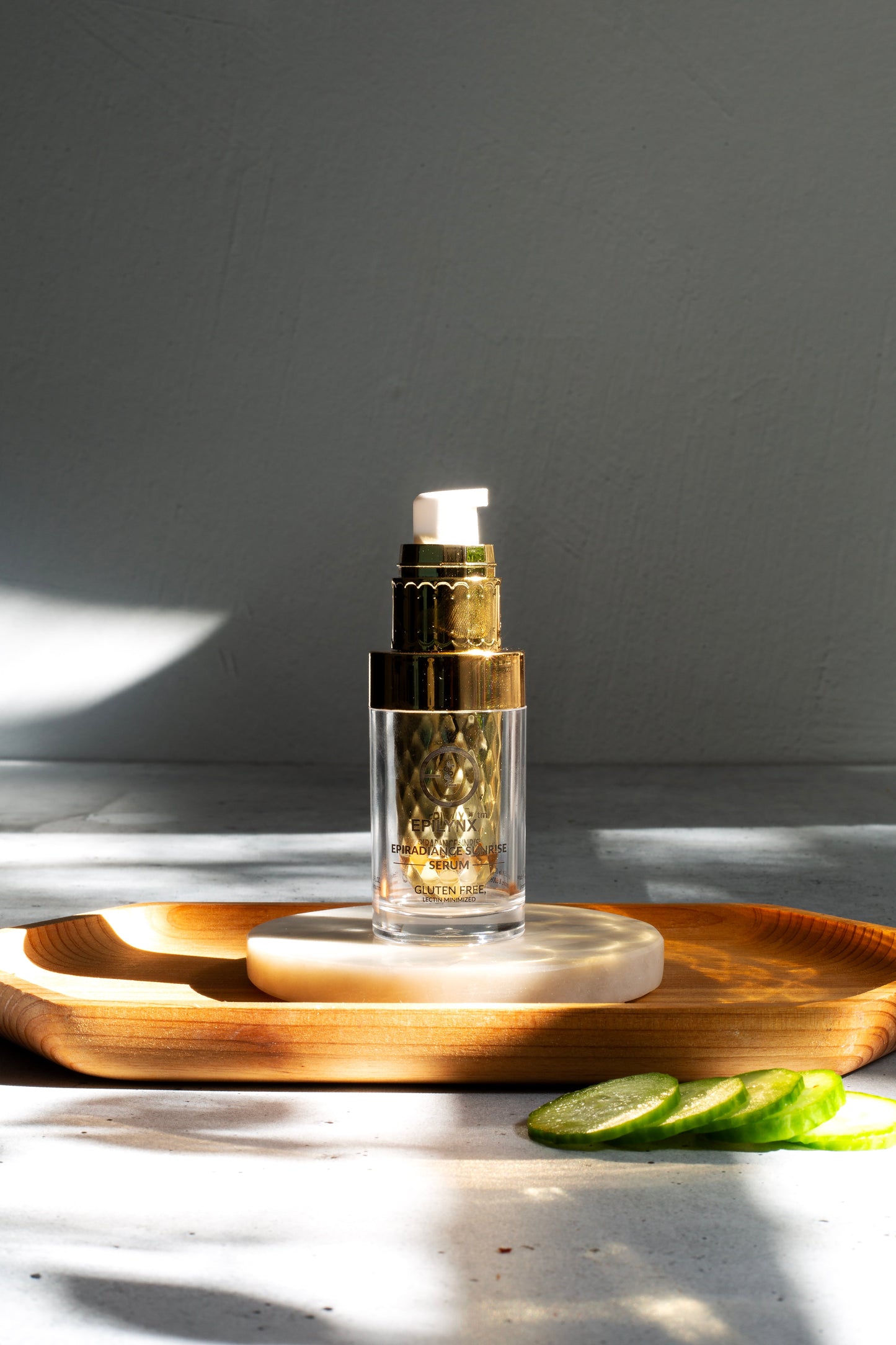 Glass serum bottle with gold pump on a round stand with green leaf pieces.
