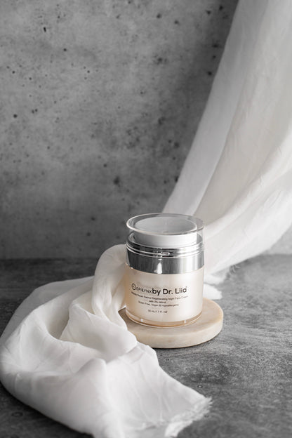 Night cream jar with silver lid on a pedestal, with white tissue beside it.