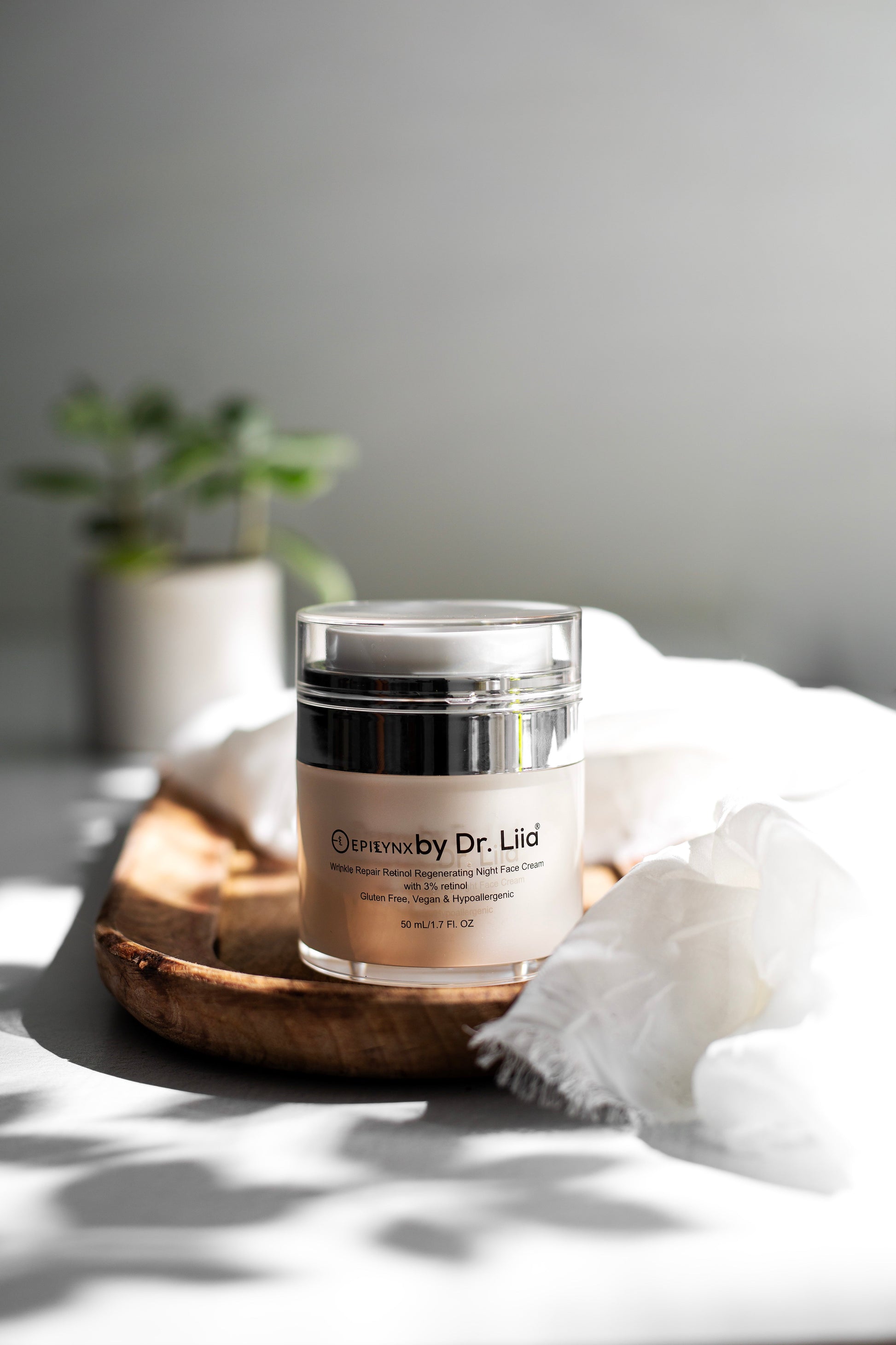 Night cream jar with silver lid on a wooden base, with white tissue nearby.