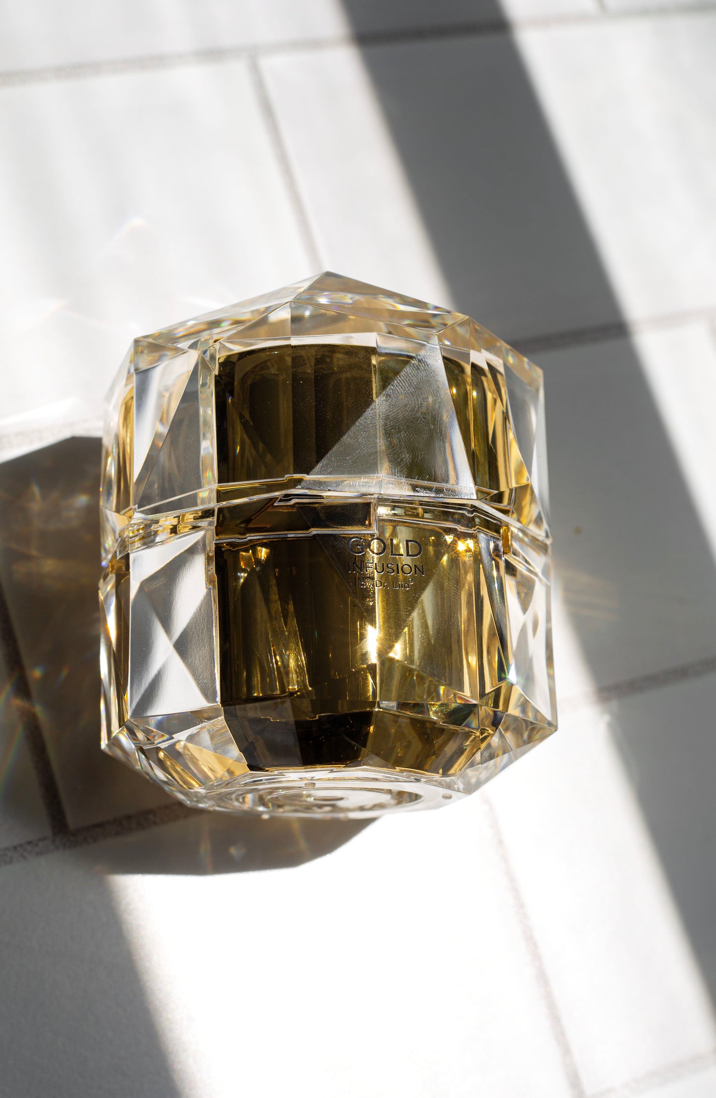Clear faceted gold infusion face cream jar on light surface, label on front