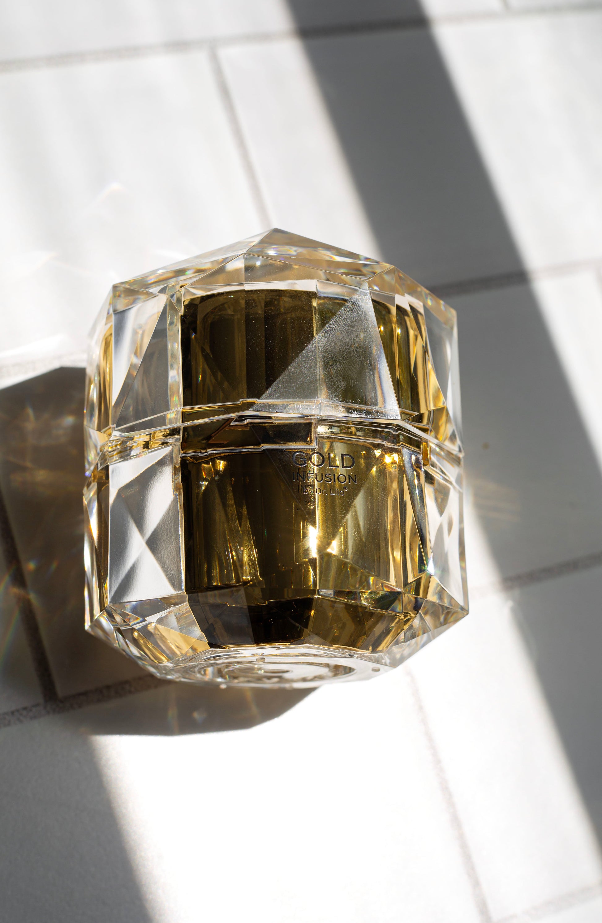 Clear faceted gold infusion face cream jar on light surface, label on front