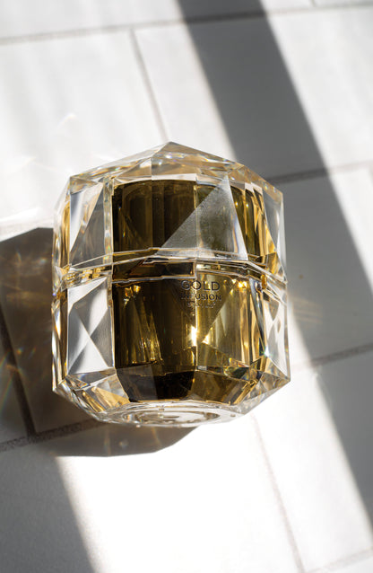 Clear faceted gold infusion face cream jar on light surface, label on front