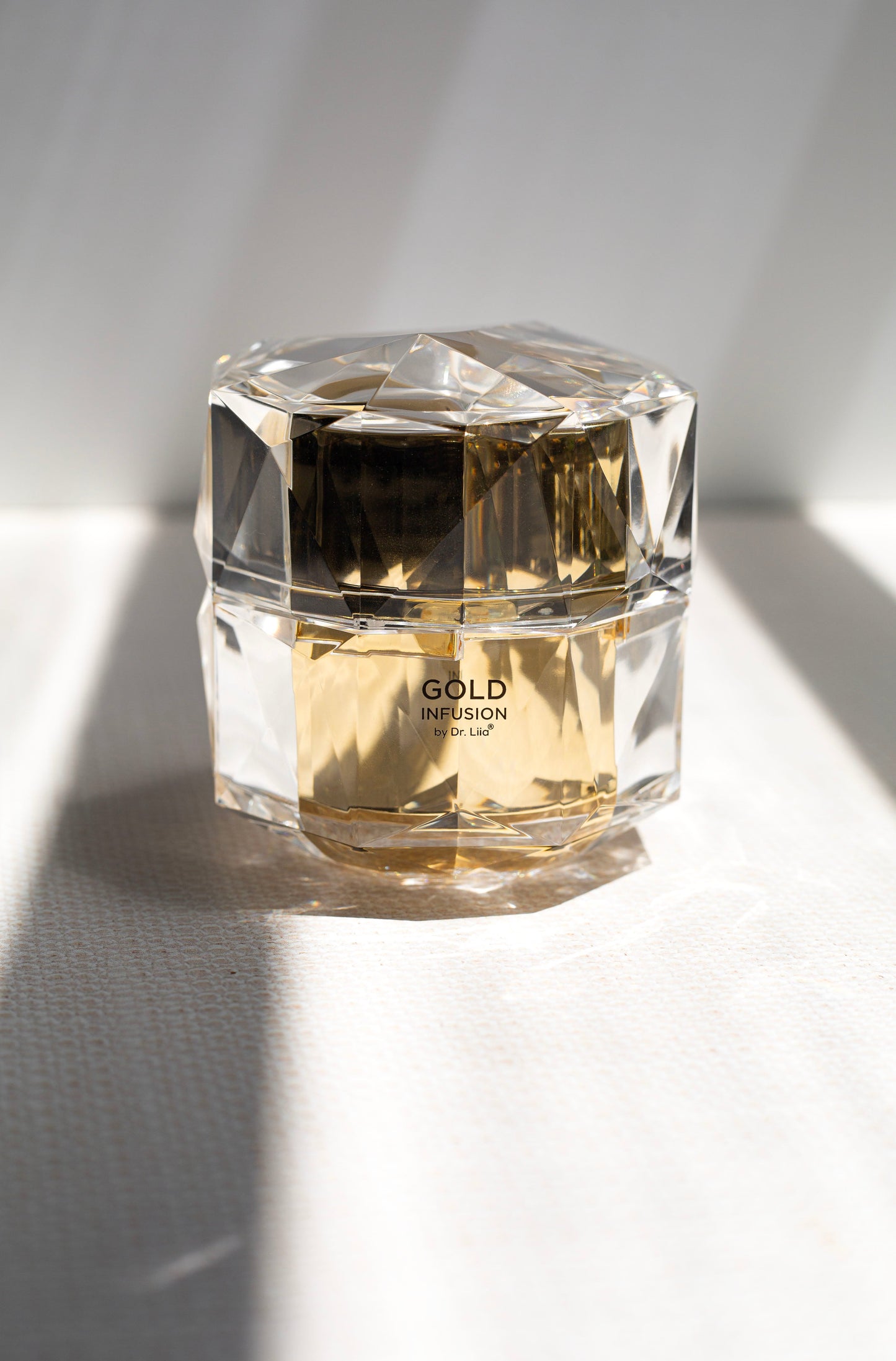 Gold infusion face cream jar in clear faceted container on white cloth