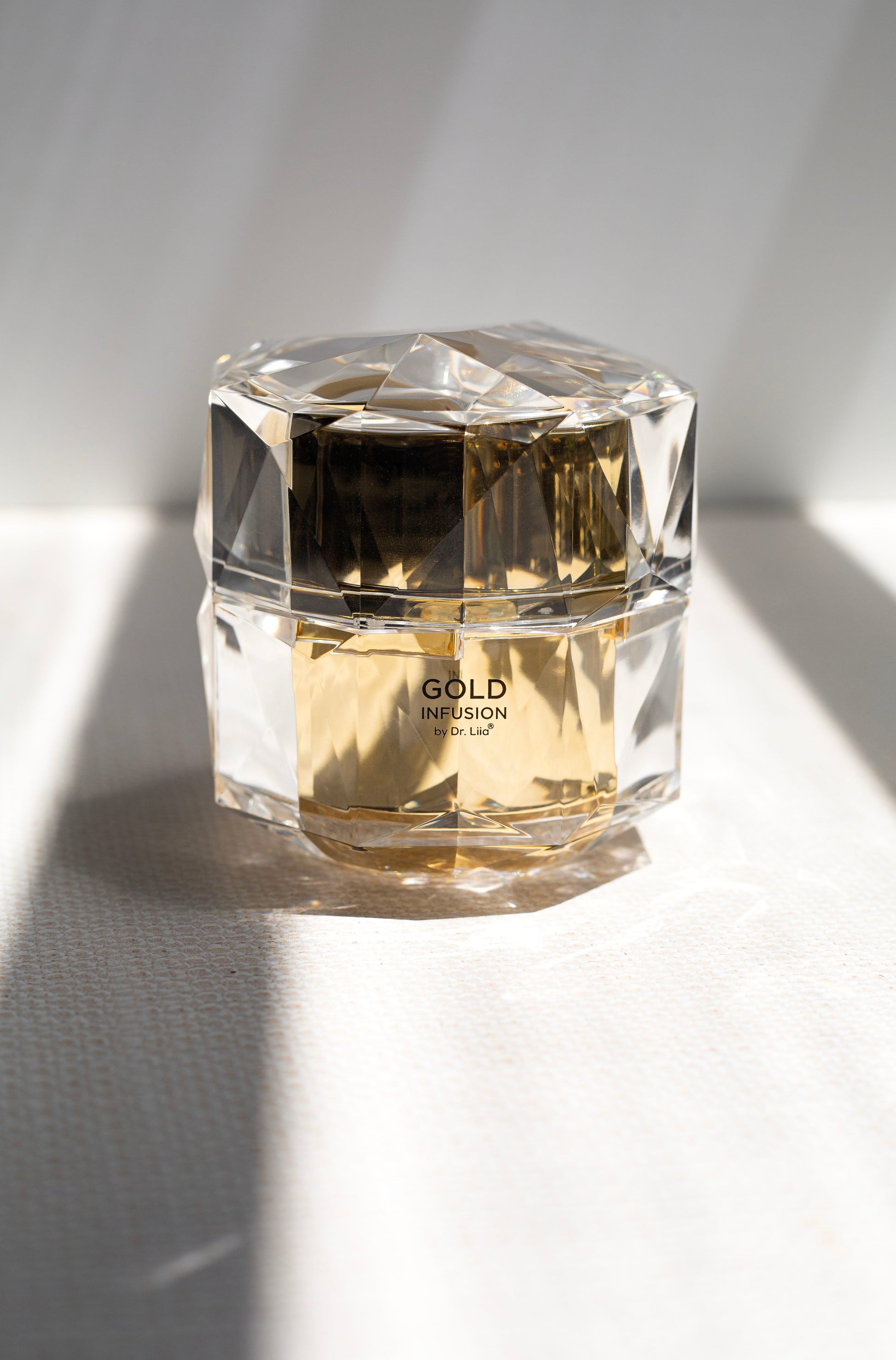 Gold infusion face cream jar in clear faceted container on white cloth
