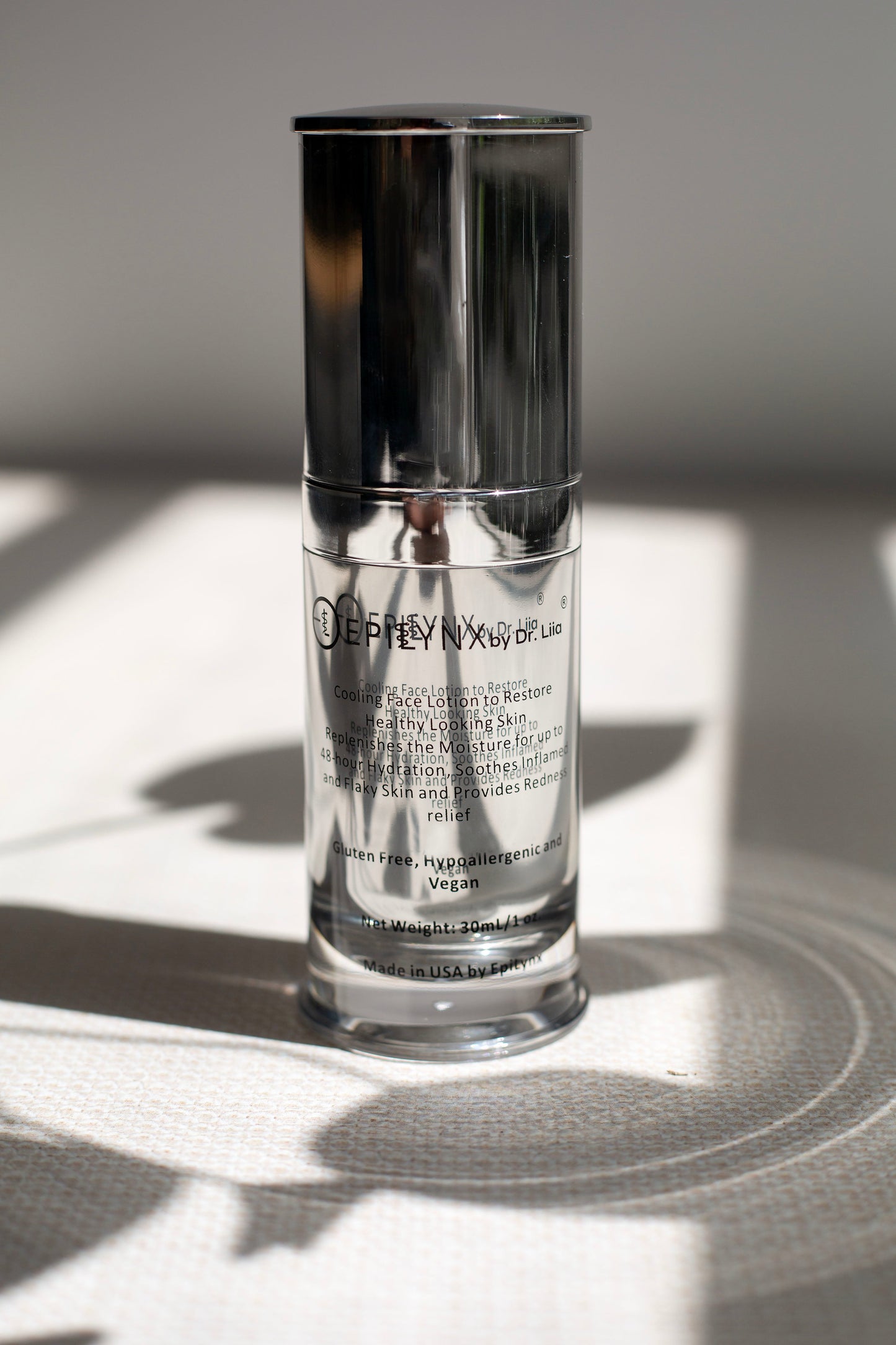 Clear glass face moisturizer bottle with chrome pump and silver cap label