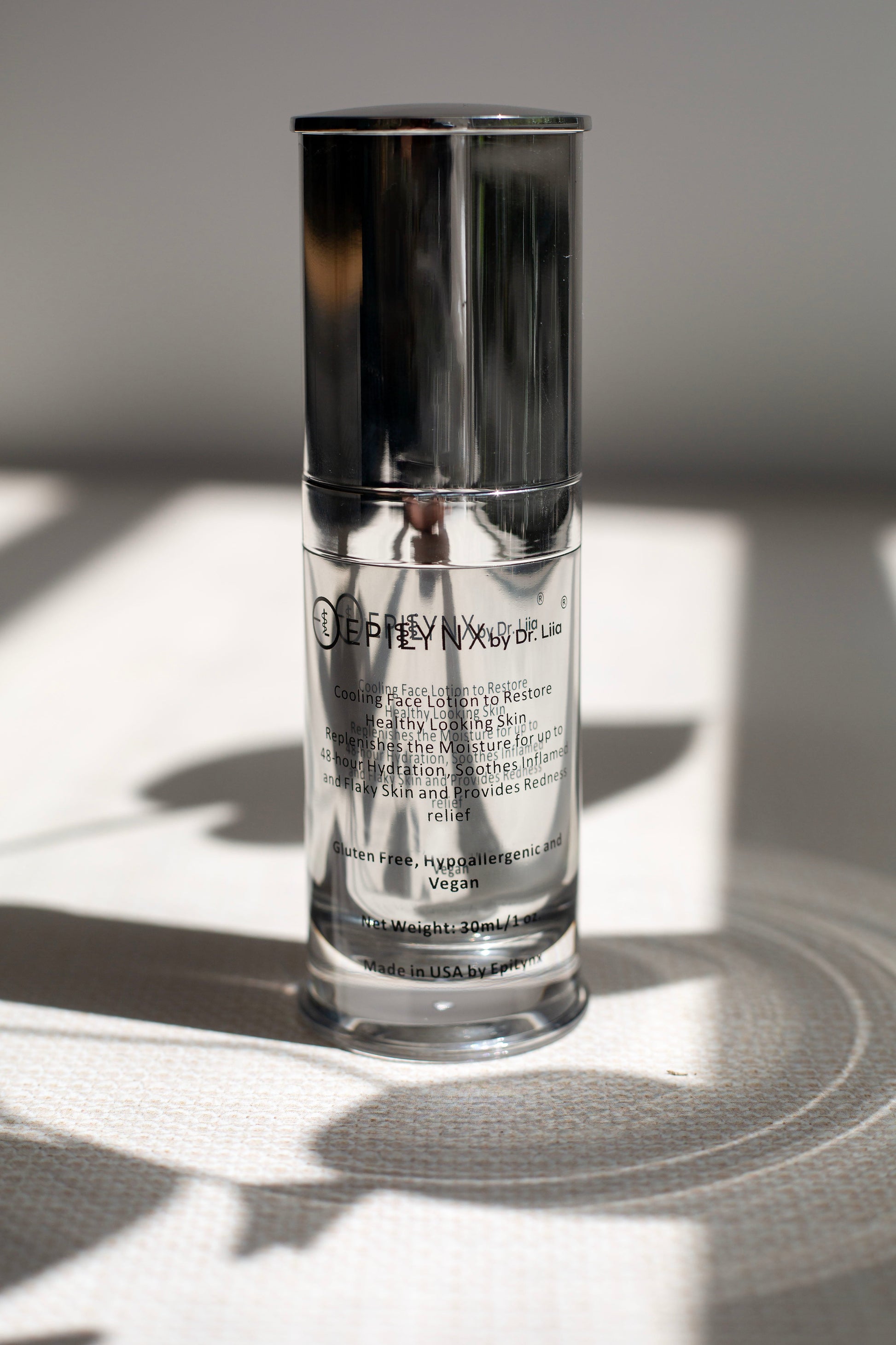 Clear glass face moisturizer bottle with chrome pump and silver cap label
