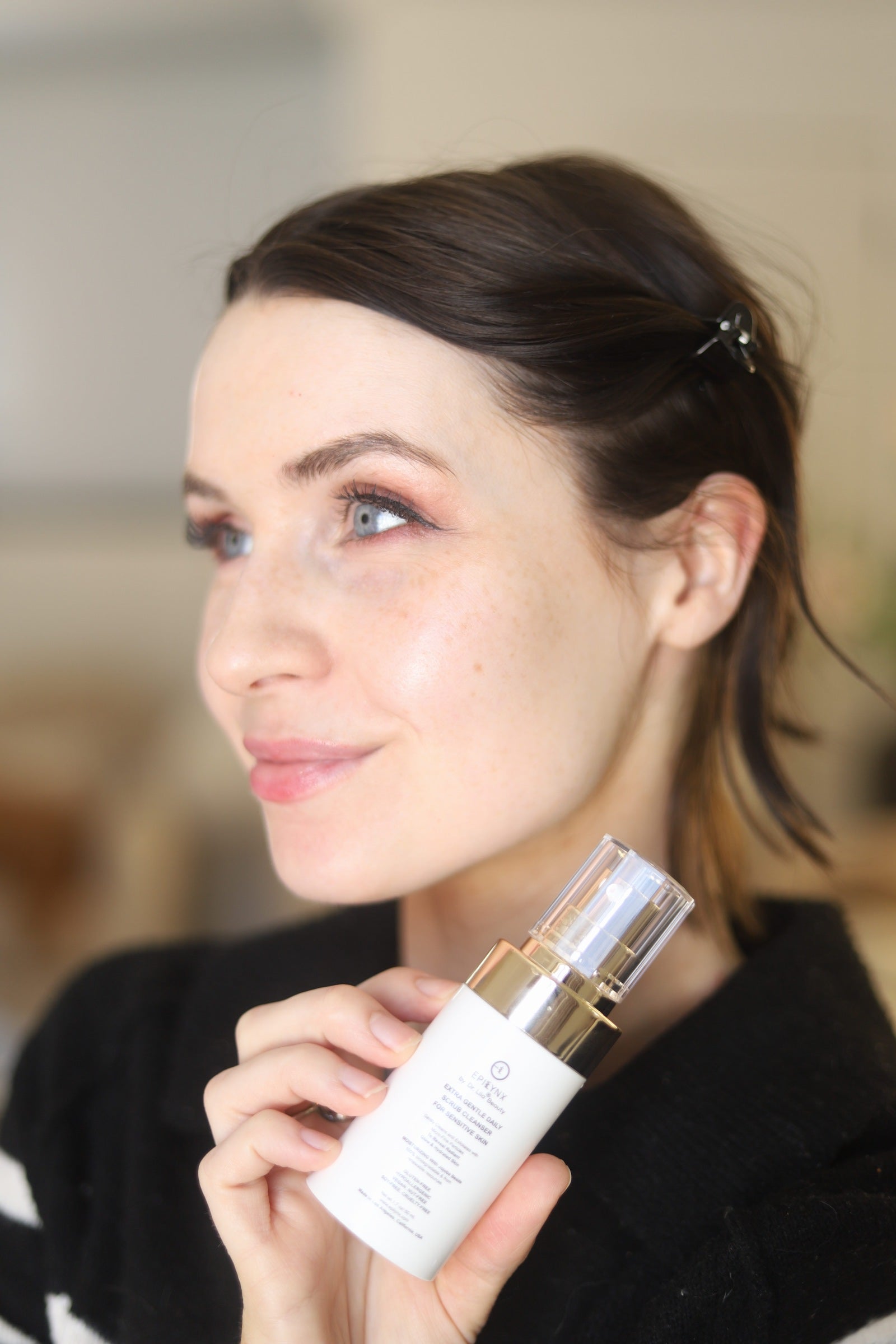 Woman holding a face scrub cleanser bottle with clear cap and gold pump