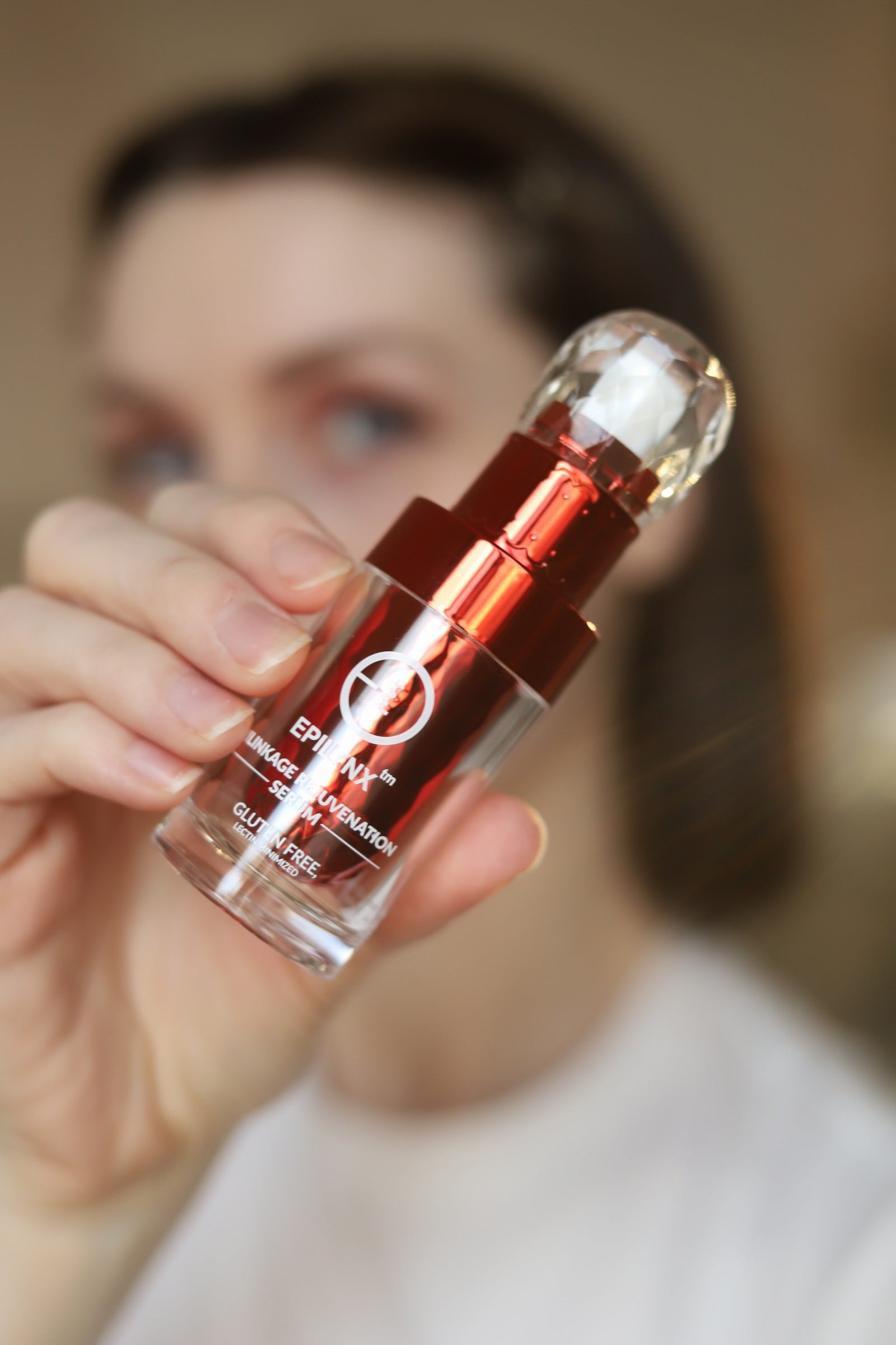 Face serum bottle held close to camera by hand with red cap