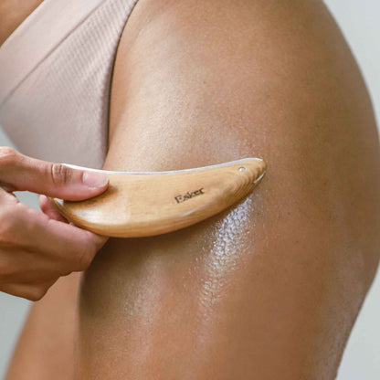 Wood body exfoliator tool with silver edge held against bare leg for exfoliating