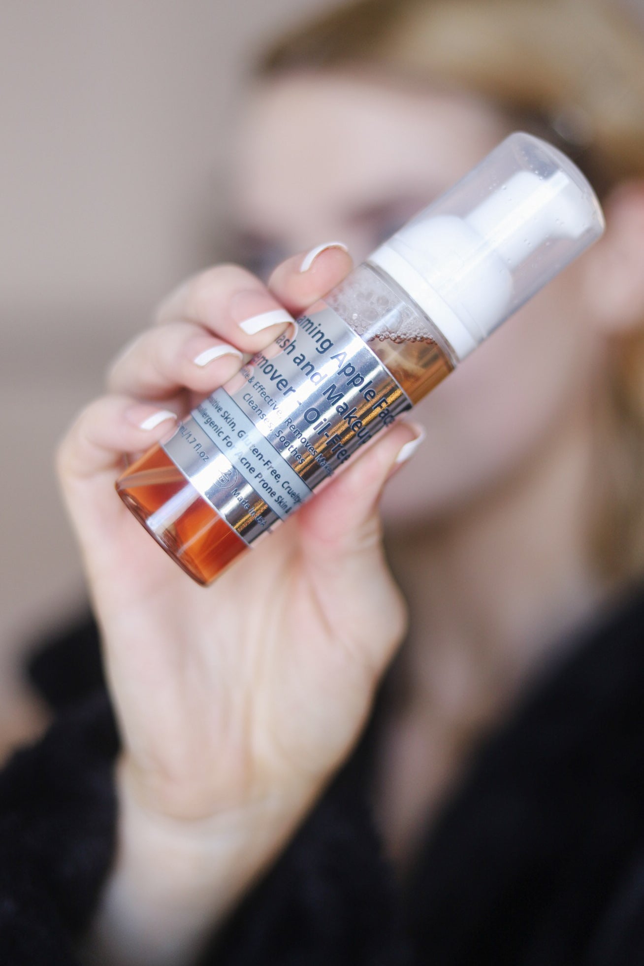 Skincare foaming cleanser bottle held in hand with white pump