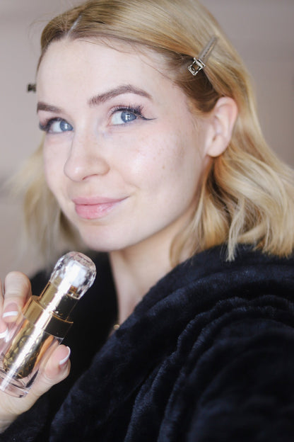 Woman holding foaming cleanser pump bottle near cheek