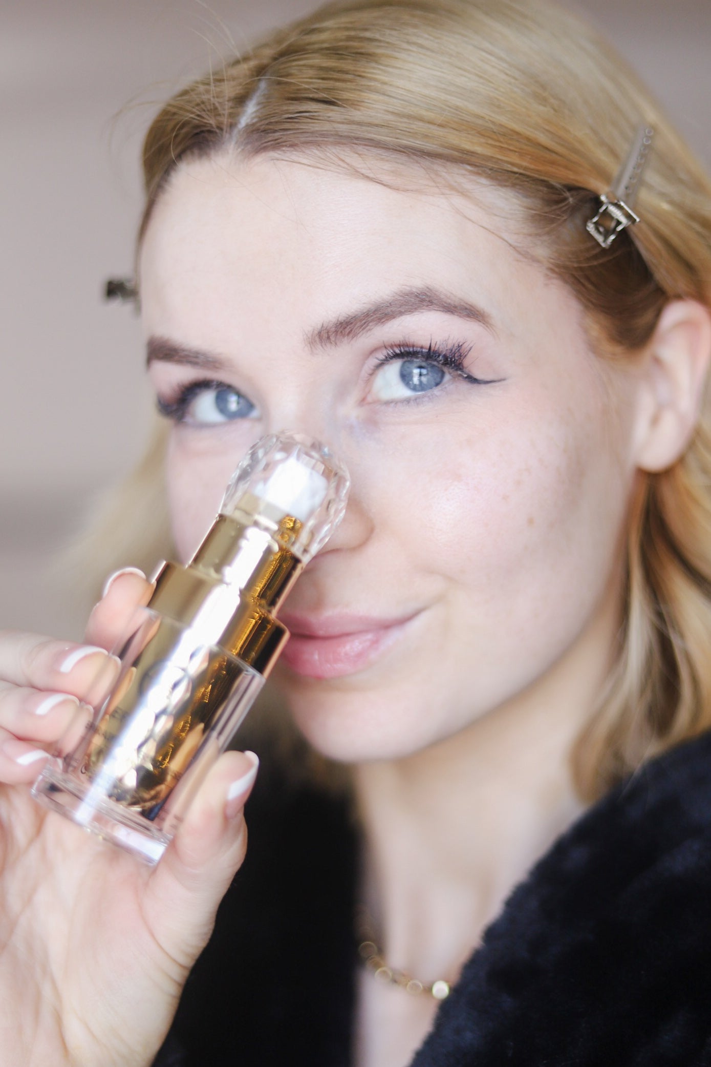 Woman applying serum from a gold pump bottle near her cheek.