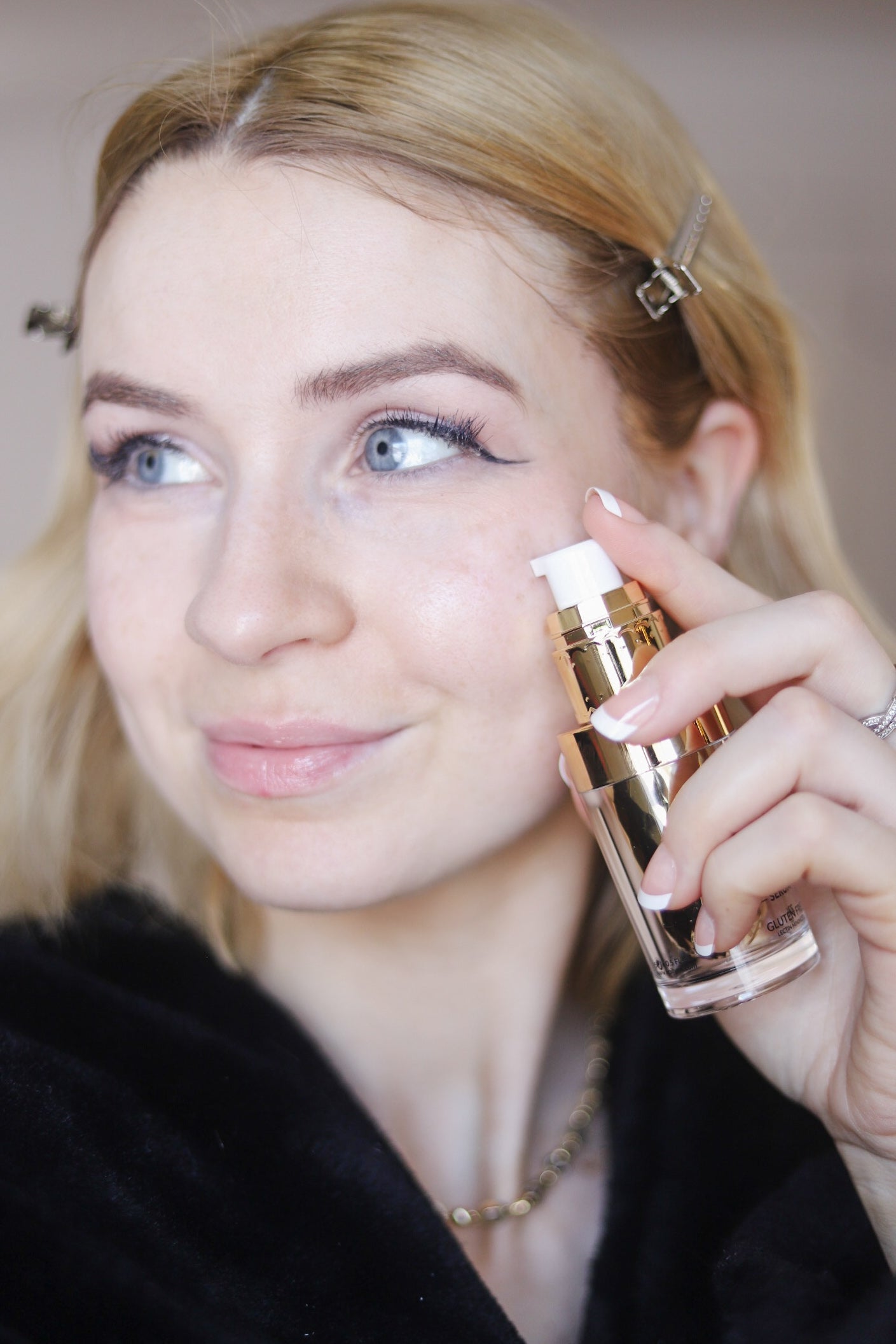 Skincare application: gold-capped serum bottle held near cheek