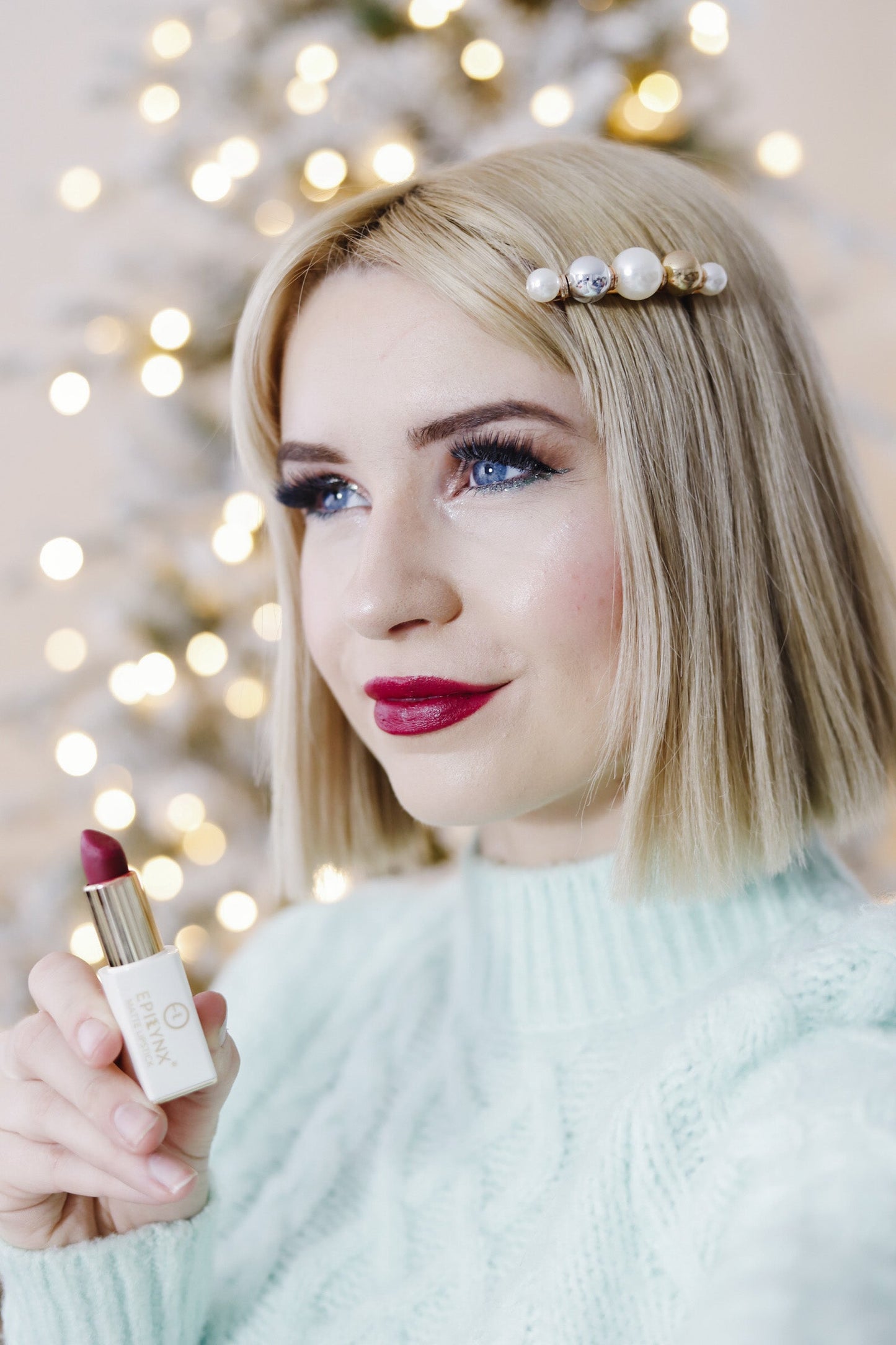 Matte lipstick in gold tube and white case with deep red shade, held by a model.
