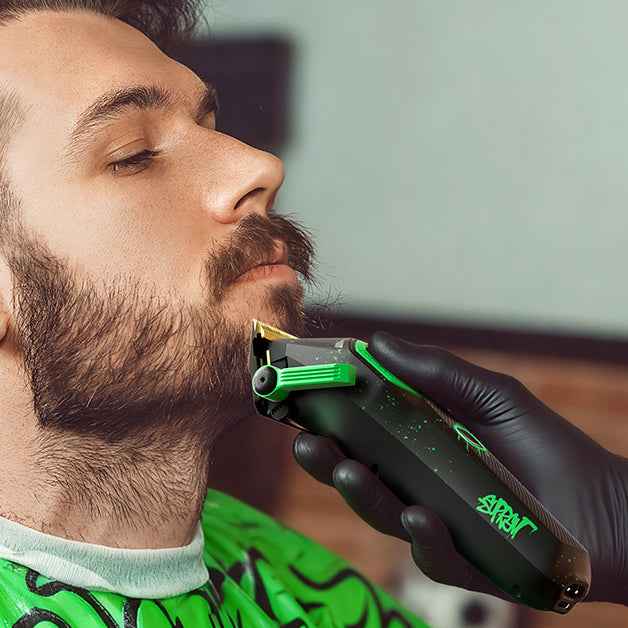 Hair clipper held near beard with black-and-green trimmer head and guard.