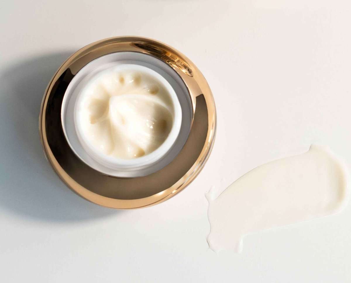 Open under-eye cream container showing thick white cream inside gold rim