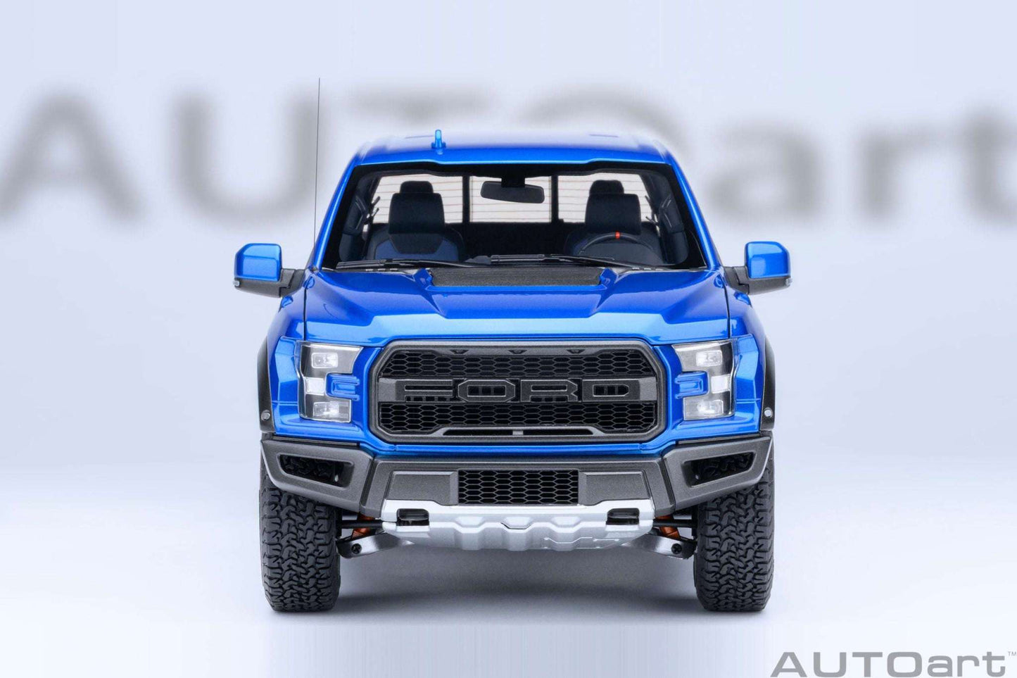 Blue pickup truck model front view with large black grille, fog lights, and knobby tires